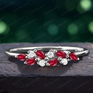 Peut inclure: Une bague en argent ornée d'un groupe de pierres précieuses rouges en forme de marquise et de pierres blanches rondes. Le design de la bague est monté sur un fin anneau, créant une apparence délicate et élégante. Les pierres sont disposées en motif floral.