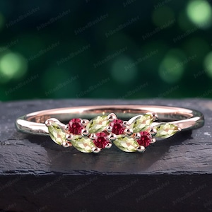 May include: A delicate rose gold band ring with a cluster of pear-shaped green and red gemstones. The ring features a repeating pattern of green and red stones.