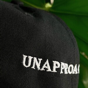 May include: Black baseball cap with white embroidered text that reads "UNAPPROACHABLE".