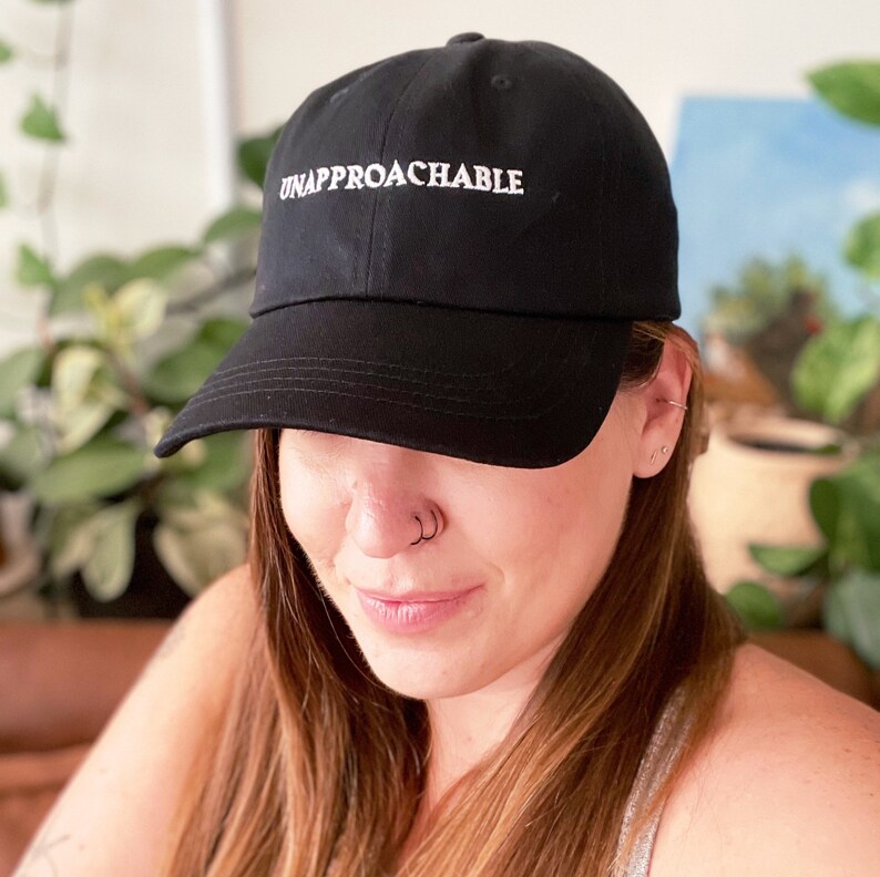 May include: A black baseball cap with white embroidery that reads "UNAPPROACHABLE".