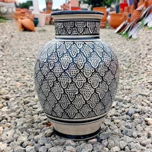 May include: A ceramic vase with a bulbous body and a narrow neck. The vase is primarily white with a detailed black pattern covering the surface. The rim and base are also black, creating a striking contrast. This decorative vase is suitable for home decor.