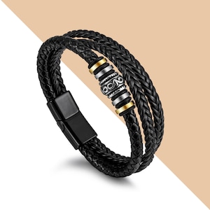 May include: A black leather bracelet with a braided design and a silver and gold bead with an intricate pattern.