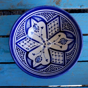 Peut inclure: Un bol en céramique blanche avec un motif géométrique bleu et blanc. Le bol est rond et a un bord large.