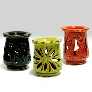 May include: Three ceramic candle holders in black, green, and red-orange. Each has a unique floral or leaf-like cutout design. The candle holders are cylindrical with a flared top and base, and are suitable for home decor.