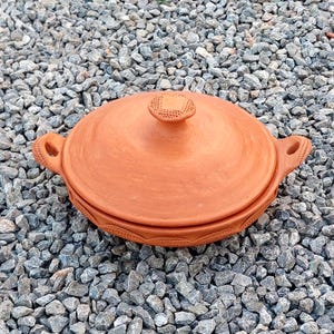 May include: A terracotta cooking pot with a lid. The pot has a decorative design around the rim and a knob on the lid.