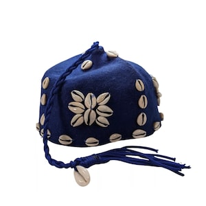 Puede incluir: Un sombrero de fieltro azul con un diseño de conchas blancas y una borla azul. El sombrero está decorado con conchas blancas.