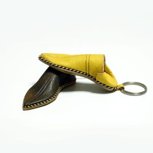 Peut inclure: Un porte-clés en forme de pantoufle en cuir jaune avec une pantoufle en cuir marron attachée à un anneau de clé argenté.