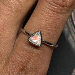 Peut inclure: Une bague en argent ornée d'une pierre précieuse triangulaire et irisée. La pierre précieuse reflète un spectre de couleurs, dont le rose et l'orange. La bague a un fin anneau poli.