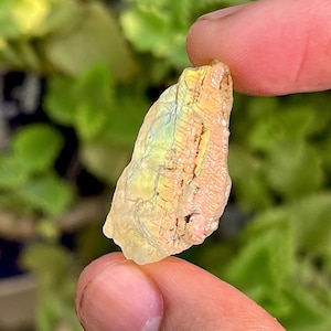 May include: A small, iridescent, clear and white, rough-cut, natural gemstone with a rainbow sheen.