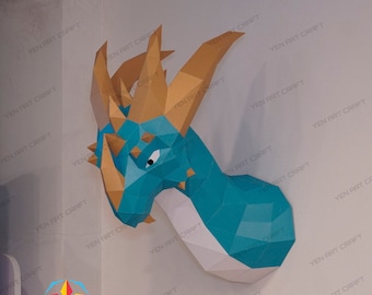 May include: A papercraft dragon head sculpture with a teal blue, white, and gold color scheme. The dragon has a large, pointed horn and a fierce expression.