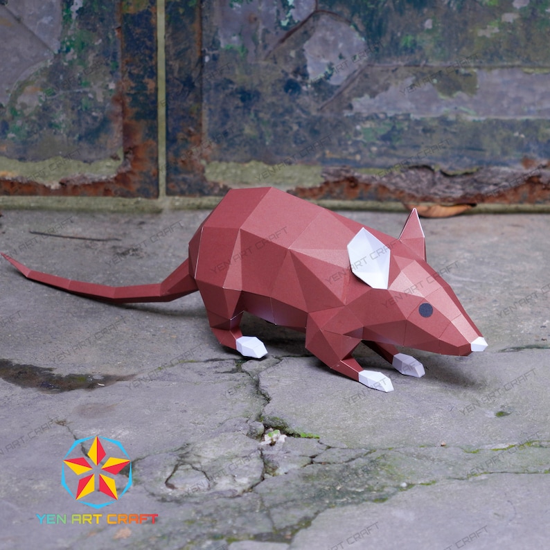 May include: A brown papercraft mouse with white ears and a black eye. The mouse is posed on a cracked concrete surface.