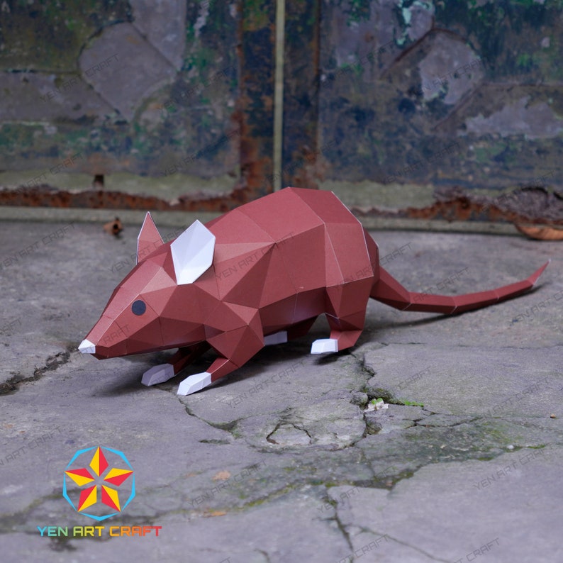 May include: A brown papercraft mouse with white ears and a long tail. The mouse is posed in a walking position on a gray concrete surface.