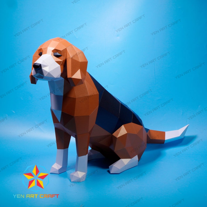 Puede incluir: Un modelo de papel de un perro beagle sentado con la cabeza inclinada hacia abajo. El perro est&aacute; hecho de papel marr&oacute;n, negro y blanco y tiene un aspecto realista.