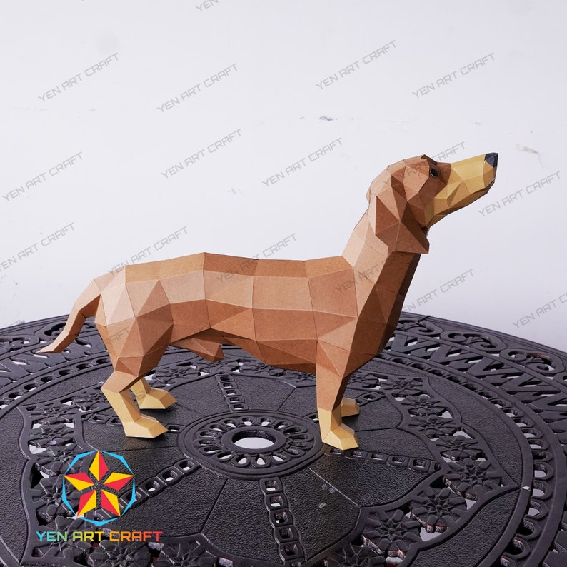 May include: A brown papercraft dachshund model standing on a black circular table with a decorative pattern. The model is made of folded paper and has a realistic appearance.