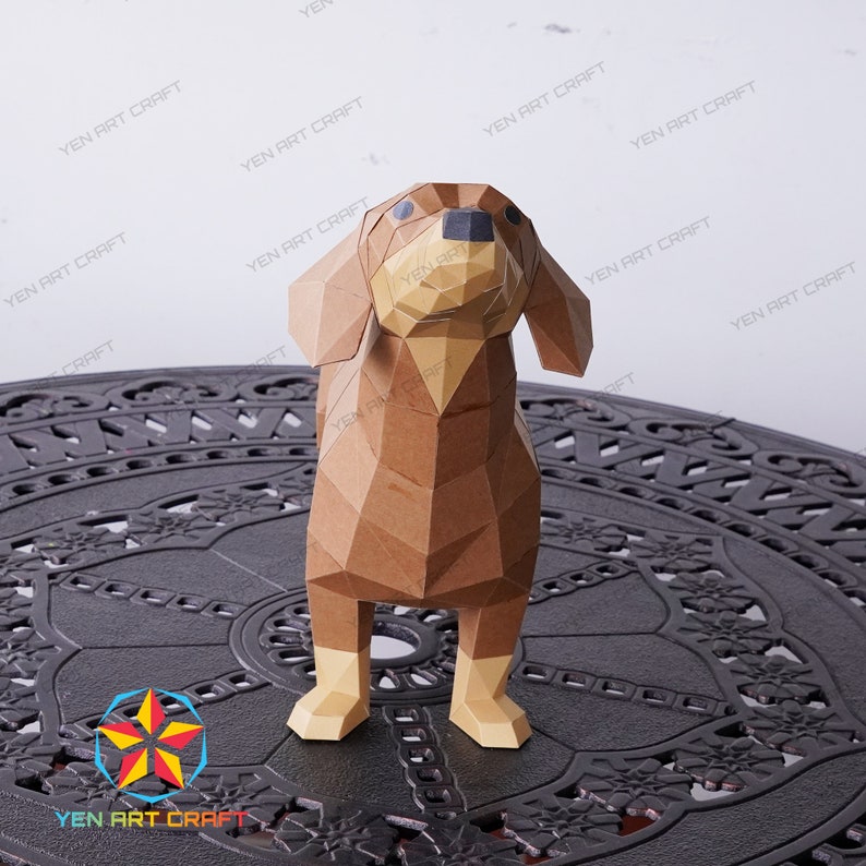 May include: A brown papercraft dachshund dog model standing on a black metal table with a decorative design. The dog is looking up with its head tilted.