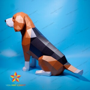 Puede incluir: Un modelo de papel de un perro beagle sentado con la cola enroscada. El perro est&aacute; hecho de papel marr&oacute;n, negro y blanco y tiene un aspecto realista.