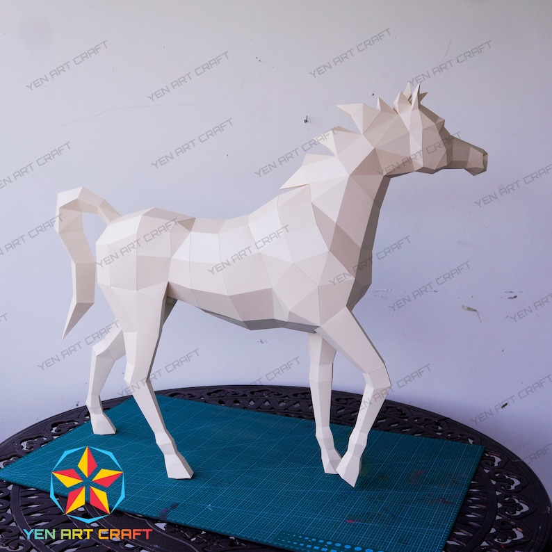 May include: A white papercraft model of a horse, standing on a table with a green surface. The horse is made of many small, folded pieces of paper, creating a geometric design.