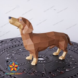 May include: A brown papercraft dachshund model, standing on a black metal table with a decorative design. The dachshund is looking up and has a long, thin body.