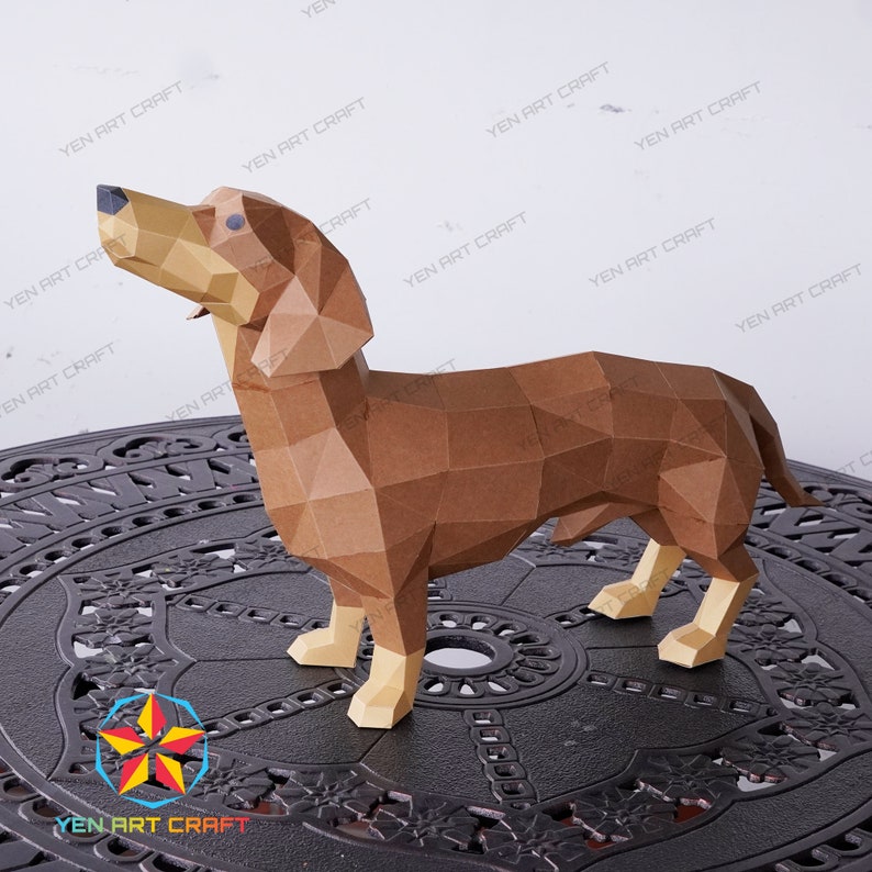 May include: A brown papercraft dachshund model, standing on a black metal table with a decorative design. The dachshund is looking up and has a long, thin body.