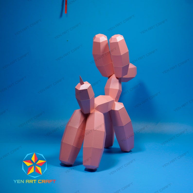 May include: A pink paper sculpture of a balloon dog, with geometric shapes and a pointed horn. The dog is set against a blue background. The text "YEN ART CRAFT" is visible in the image.
