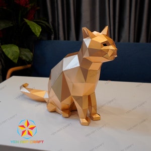 Pu&ograve; includere: Un modello di carta di un gatto dorato seduto con la coda arrotolata intorno alle zampe. Il gatto &egrave; fatto di molti piccoli triangoli che creano uno schema geometrico.