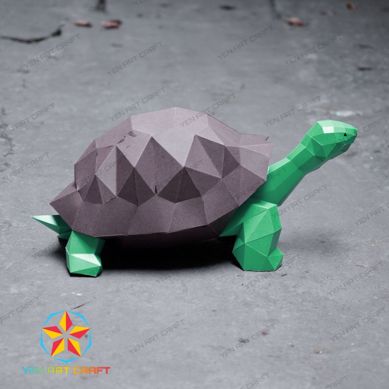 Puede incluir: Un modelo de tortuga de papel artesanal de color verde y marr&oacute;n. La tortuga est&aacute; hecha de papel doblado y tiene un aspecto realista. La tortuga est&aacute; de pie sobre una superficie gris.