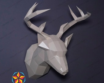 May include: A gray papercraft deer head with large antlers mounted on a dark gray wall. The deer head is made of folded paper and has a realistic appearance.