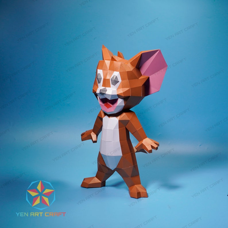 May include: A brown and white papercraft model of Tom from the cartoon Tom and Jerry. The model is standing on a blue surface and has a large, pink ear.