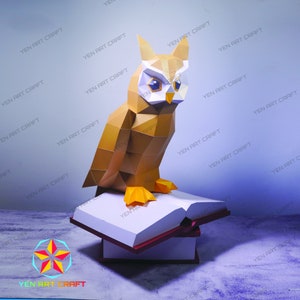 May include: A papercraft owl perched on top of a stack of books. The owl is brown and yellow with large, white eyes. The books are white with red spines.
