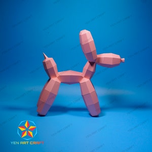 May include: A pink papercraft balloon dog stands against a blue background. The dog is constructed from geometric shapes, with a pointed ear and a curled tail. The image has the text "YEN ART CRAFT" repeated around the edges.