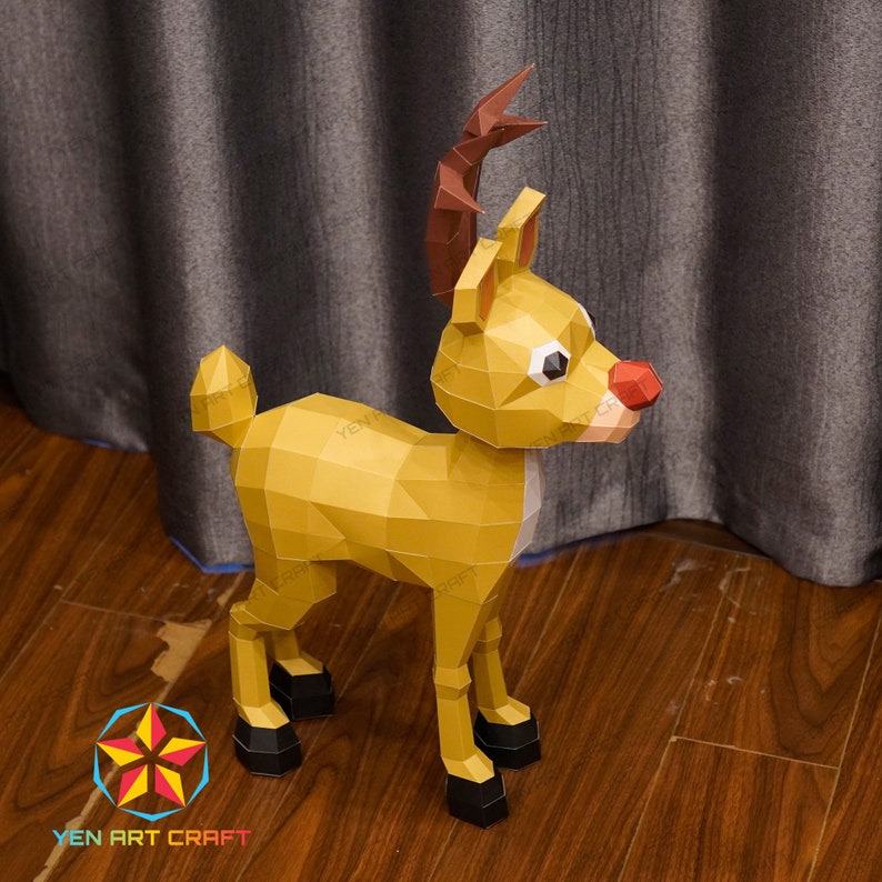 May include: A papercraft reindeer model with brown antlers, a red nose, and black hooves. The reindeer is standing on a wooden floor.