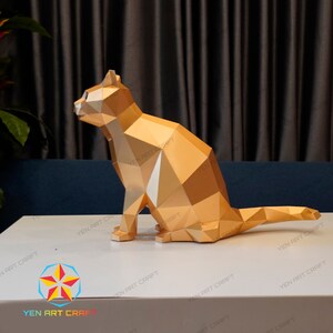 Pu&ograve; includere: Un modello di carta di un gatto seduto con la coda arrotolata dietro di lui, di colore dorato. Il gatto &egrave; fatto di molti piccoli triangoli che creano un design geometrico.