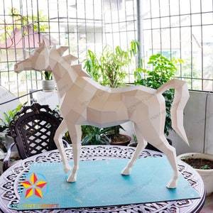 May include: A white papercraft horse sculpture with a geometric design. The sculpture is standing on a blue cutting mat on a wooden table.