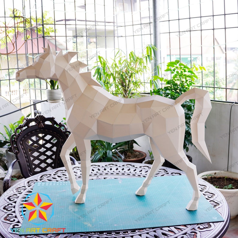 May include: A white papercraft horse sculpture with a geometric design. The sculpture is standing on a blue cutting mat on a wooden table.