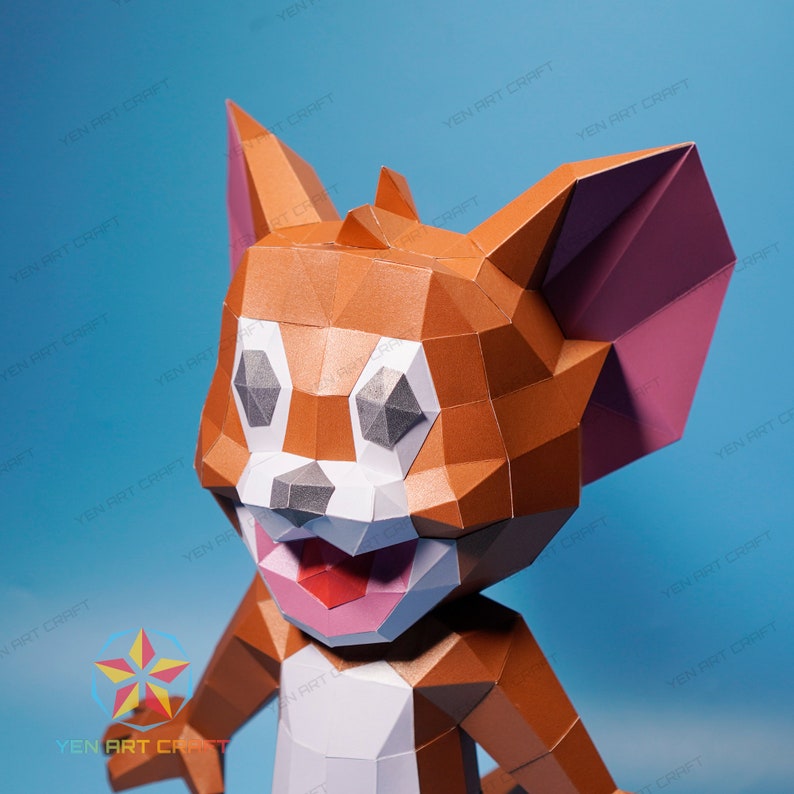 May include: A papercraft model of Tom from the cartoon Tom and Jerry. The model is made of orange, gray, white, and pink paper. The model is posed with its head tilted to the side and its mouth open in a smile.