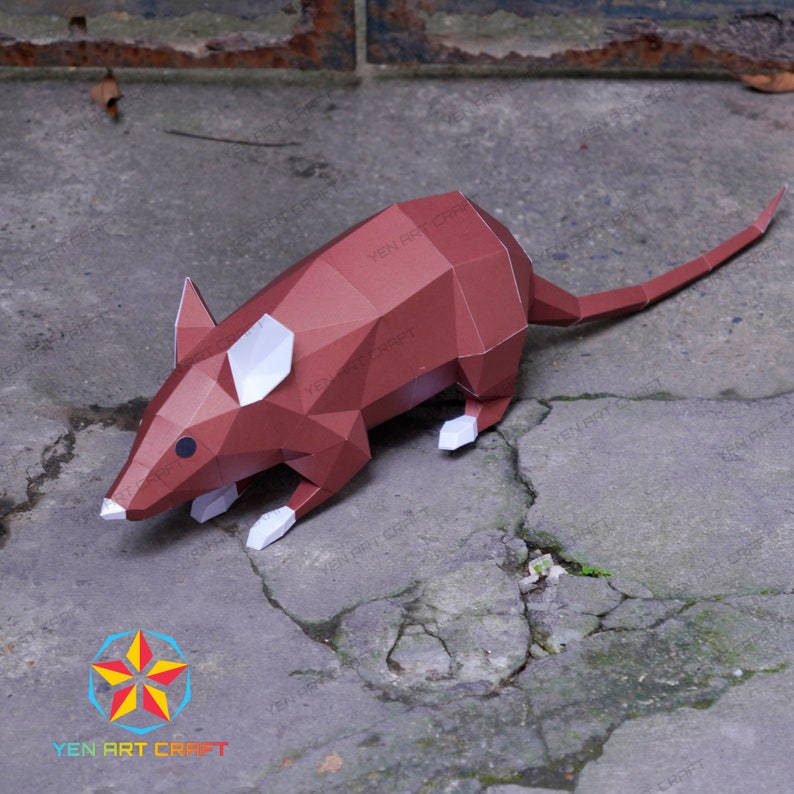 May include: A brown papercraft mouse with white ears and feet. The mouse is posed on a gray concrete surface. The image includes the text "YEN ART CRAFT" in a starburst design.
