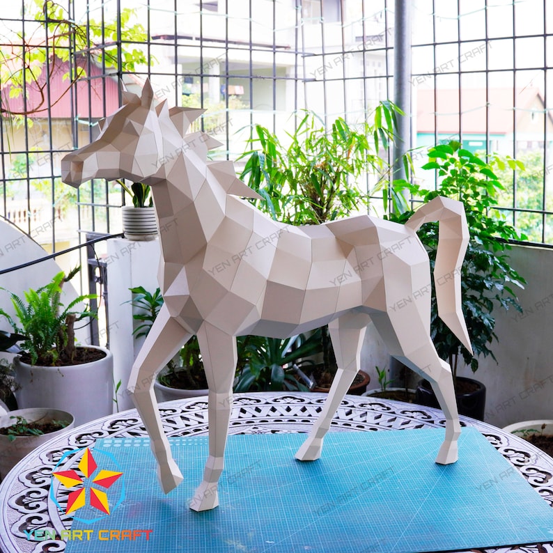 May include: A white papercraft horse model with a geometric design. The horse is standing on a blue cutting mat with a white grid pattern.