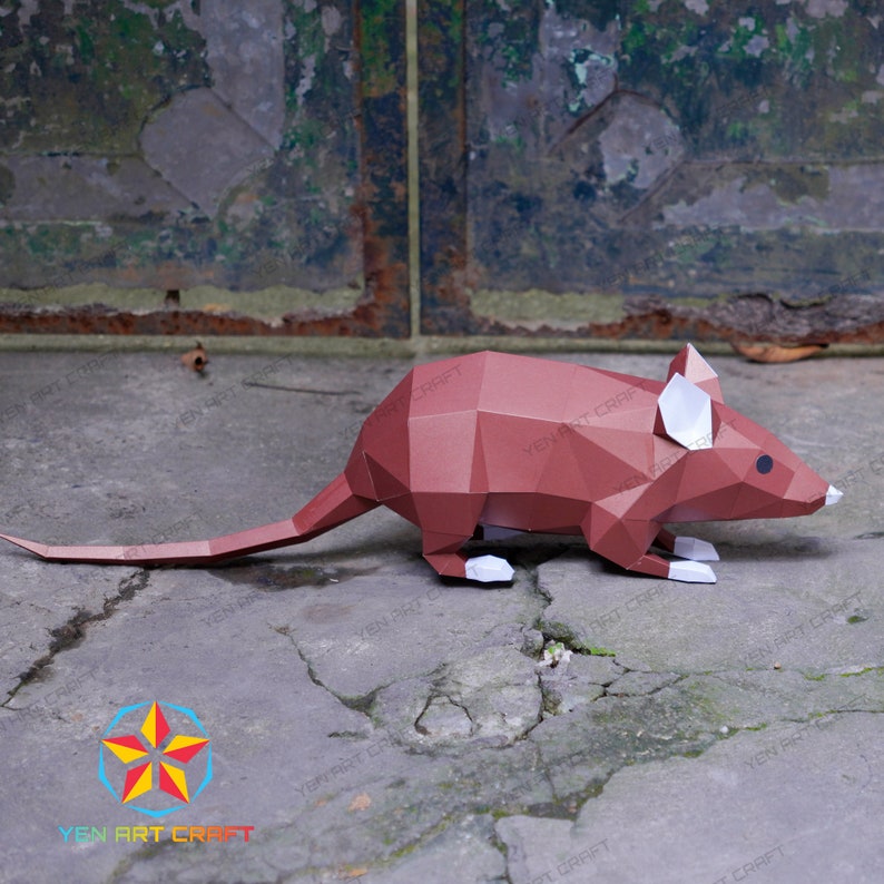 May include: A brown papercraft mouse with white ears and a long tail. The mouse is sitting on a gray concrete surface.