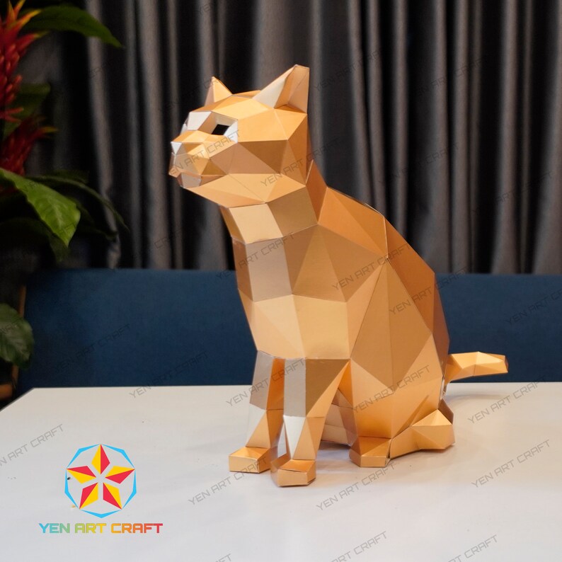 Pu&ograve; includere: Un modello di carta di un gatto dorato seduto con la coda arrotolata intorno alle zampe. Il gatto &egrave; fatto di molti piccoli triangoli, che gli conferiscono un aspetto geometrico.