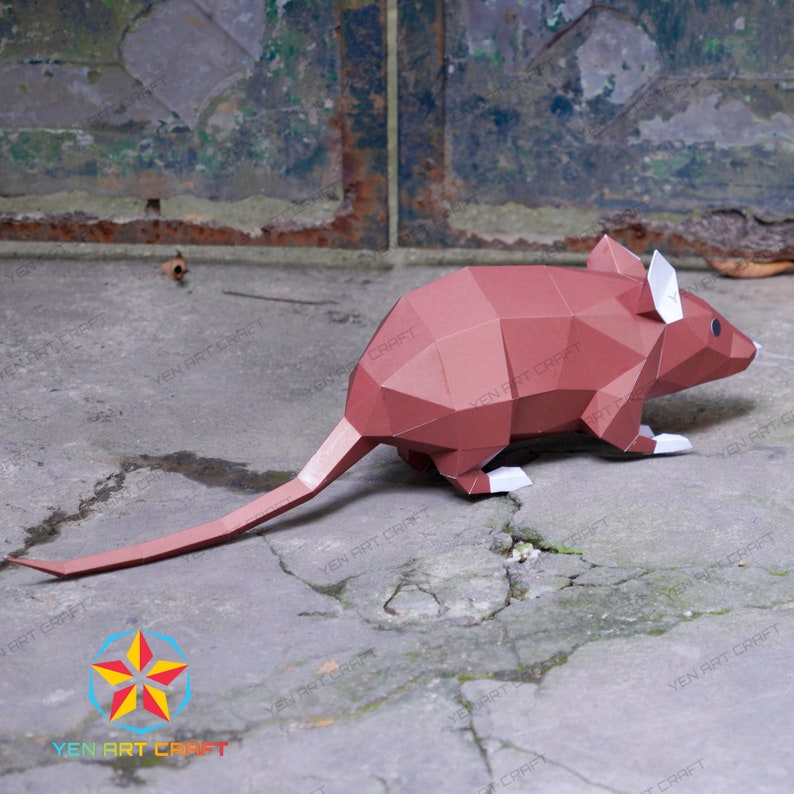 May include: A brown papercraft mouse with a long tail, standing on a cracked concrete surface. The mouse has white accents on its ears and feet.