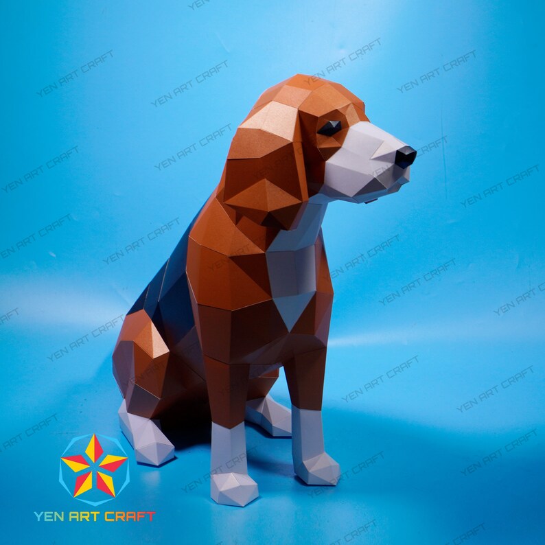 Puede incluir: Un modelo de papel de un perro beagle sentado con la cabeza girada hacia un lado. El perro es marr&oacute;n, negro y blanco. El modelo est&aacute; hecho de papel y se ensambla con pegamento.