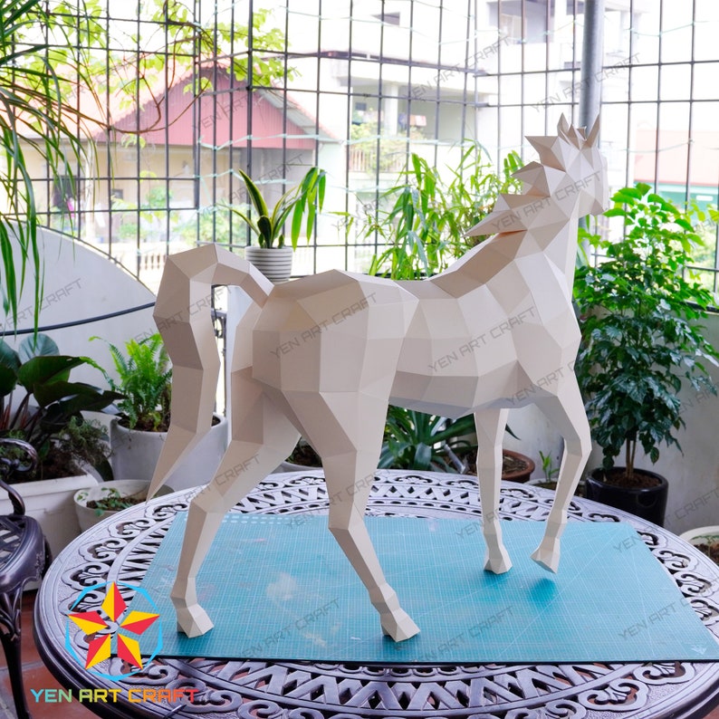 May include: A white papercraft horse model with a geometric design. The horse is standing on a blue cutting mat.