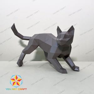 以下が含まれることがあります： グレーの幾何学的なペーパークラフトの猫の彫刻。猫は歩いているポーズで、尾が上がっています。彫刻は折り紙で作られており、多角形のデザインです。「YEN ART CRAFT」のロゴが左下にあります。