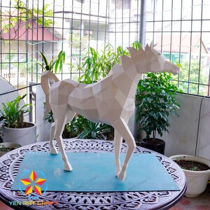 May include: A white papercraft horse sculpture with a geometric design. The sculpture is standing on a blue cutting mat on a wooden table.