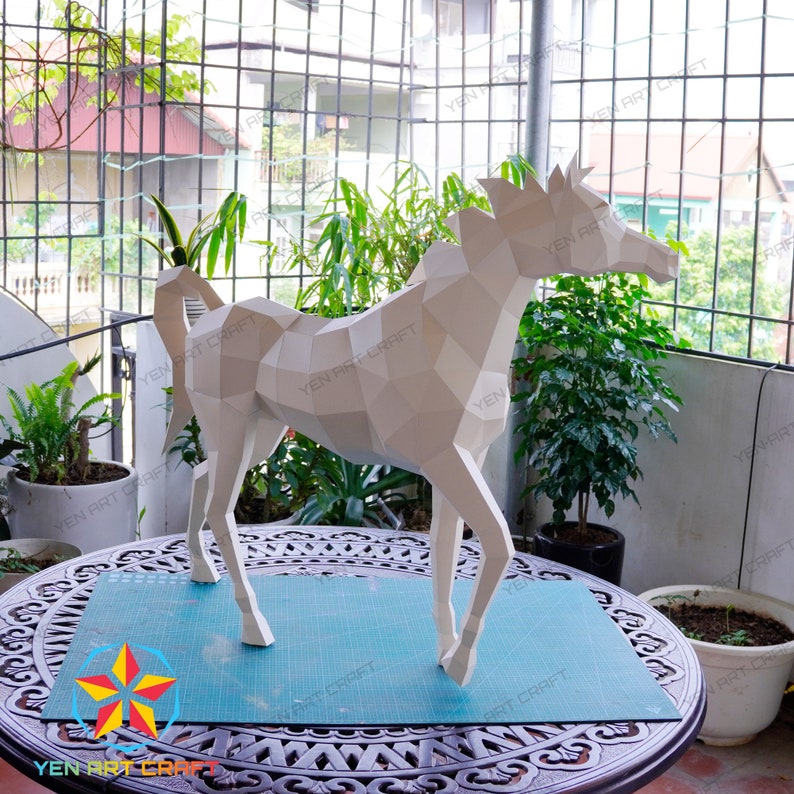 May include: A white papercraft horse sculpture with a geometric design. The sculpture is standing on a blue cutting mat on a wooden table.