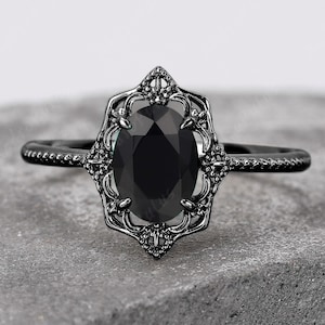 May include: Black oval engagement ring with a delicate, ornate setting. The ring is made of black metal and features a black gemstone.