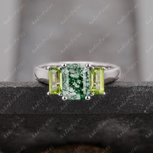 May include: A silver ring featuring a green moss agate centre stone flanked by two smaller green peridot stones.