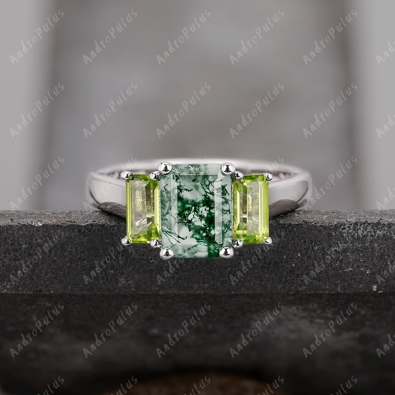 May include: A silver ring featuring a green moss agate centre stone flanked by two smaller green peridot stones.