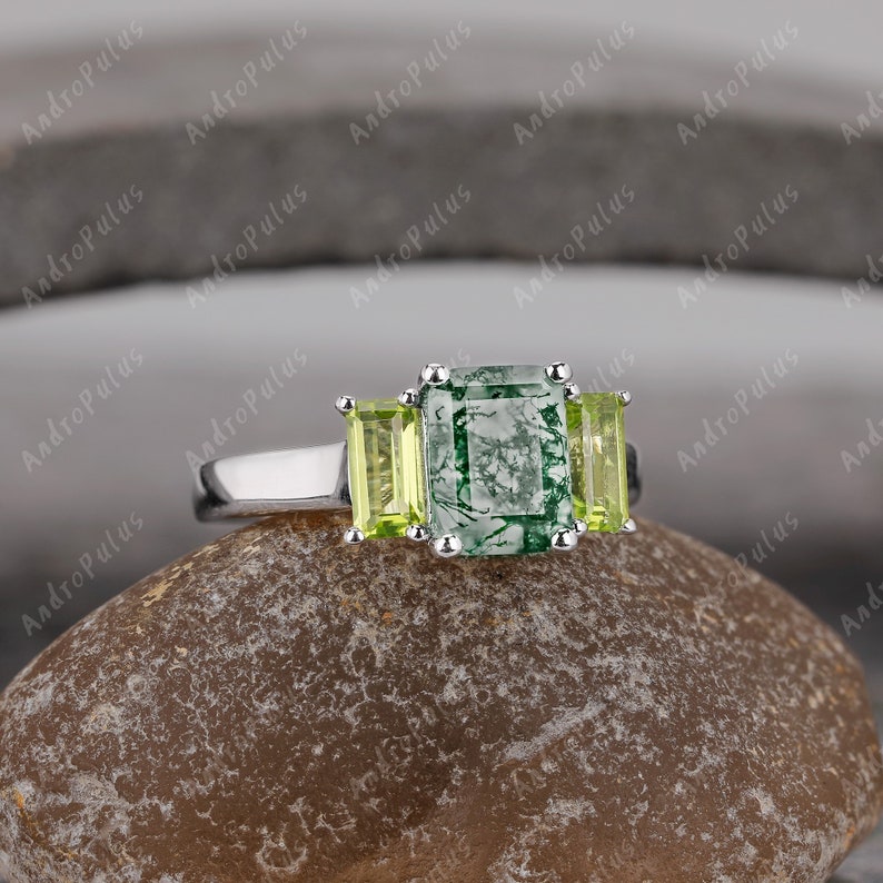 May include: A silver ring featuring three green stones. The central stone is a large, square, green agate with a white and green pattern. The two smaller stones are emerald green and rectangular.