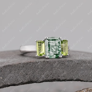 May include: A silver ring featuring a green moss agate centre stone with two smaller green stones flanking it.